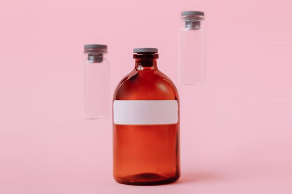 Amber glass bottle and clear stoppered vials on a pink background